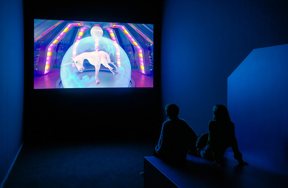 The video artwork Disco Beast is installed by projection in a blue room at the contemporary art space NRW Forum in Dusseldorf with young audience viewing on bench